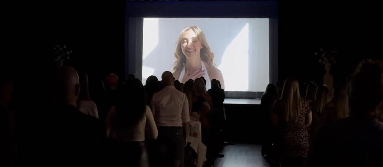 Samantha J. on screen before a full room at a live event